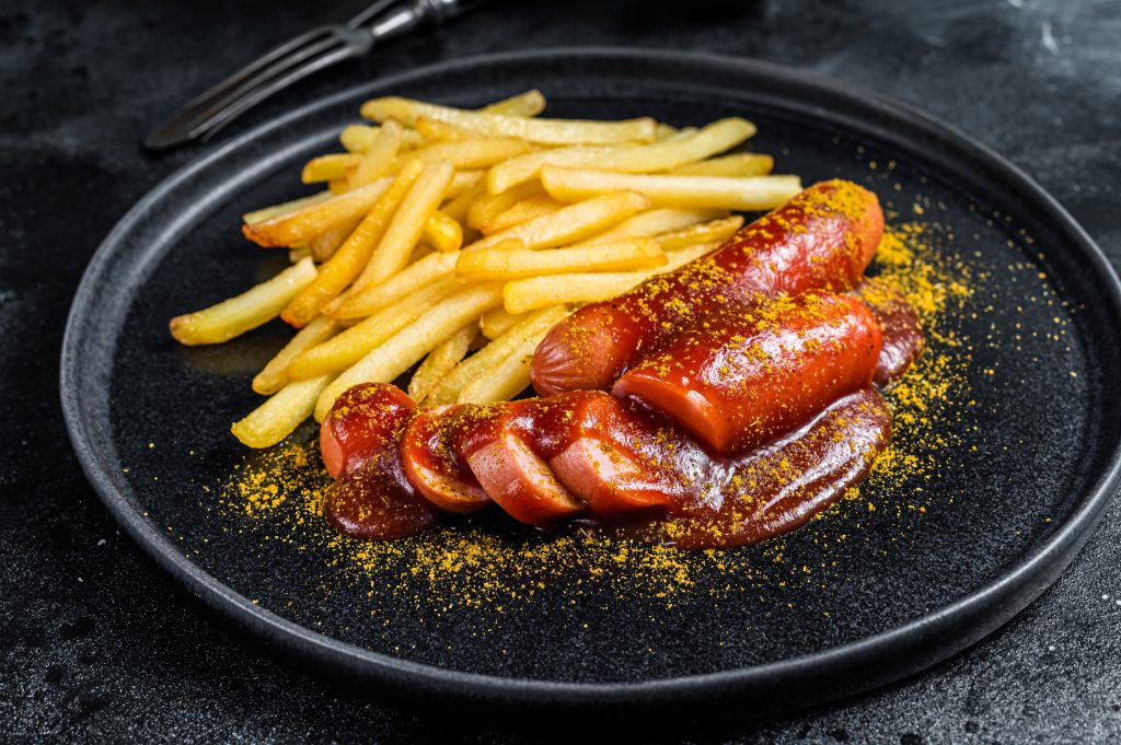 German currywurst Sausages with French fries on a plate. Black background. Top view.